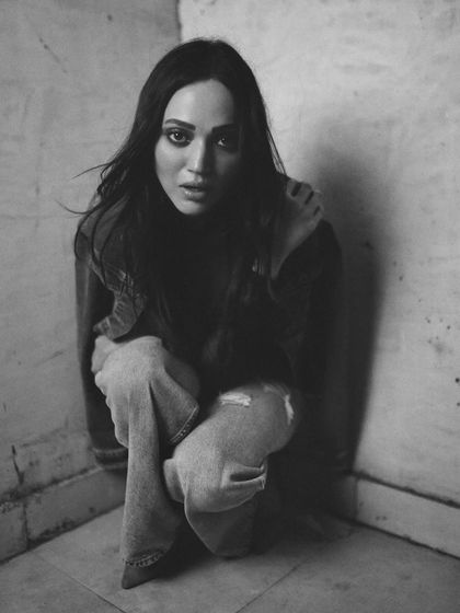 A full-body shot in a gritty, textured corner. The pose and the high-grain monochrome finish create a moody and evocative image.