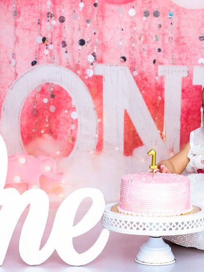 A moment of curiosity before the first bite. This photo shows the beautiful setup with the "One" sign and a lovely pink cake, ready for the birthday girl.