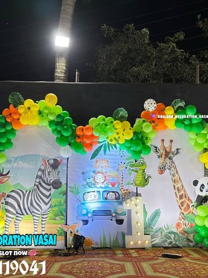 A vibrant animal theme for an outdoor night party. The setup features a large backdrop with various animals and a colorful balloon arch.