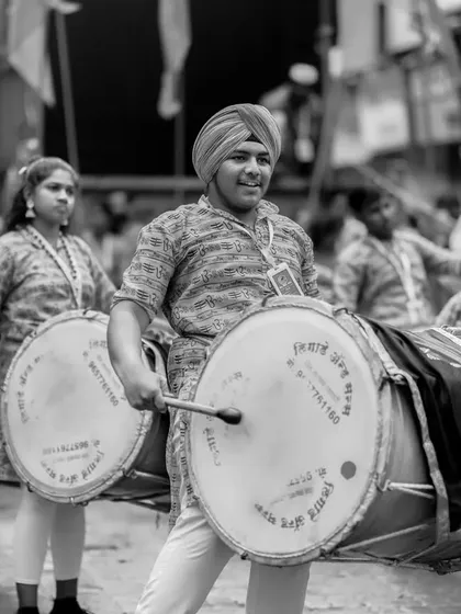 A black and white shot of a Sikh dhol player, proudly marching and playing in the procession.