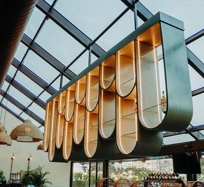 A key feature of the design is this sculptural, suspended bar shelf that hangs under a glass roof. Its curved, modular form is both a functional display and a stunning architectural statement that allows natural light to flood the space.