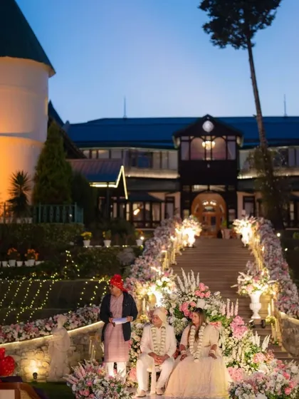 The wedding ceremony unfolds at dusk, with the couple seated before the priest against the beautifully lit facade of the hotel. This image captures the serene and spiritual atmosphere of an evening wedding in the mountains.