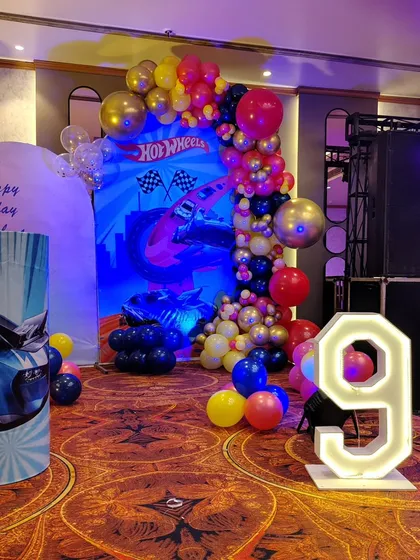 A Hot Wheels themed setup for a 9th birthday. I used a dynamic backdrop with race cars, a balloon arch in bold colors, and a large light-up number '9'.