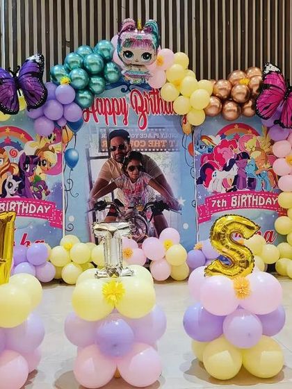 A magical butterfly and My Little Pony theme for a 7th birthday. The backdrop features a personalized photo, colorful characters, and a beautiful pastel balloon arch with large butterfly accents.