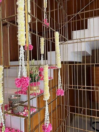 Hanging floral strings of jasmine and pink flowers are elegantly draped around a modern gold railing, demonstrating how we blend traditional elements with contemporary interior design for a unique festive look.