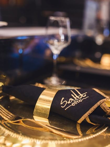 The Saltt Elite experience begins with the details. A custom-embroidered napkin and gleaming gold cutlery on a charger plate set the tone for a luxurious sit-down meal.