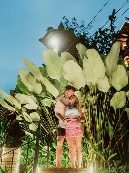 A couple embraces under the stars, surrounded by giant tropical leaves in Bali. This creative night shot captures the enchanting and exotic vibe of a destination shoot.