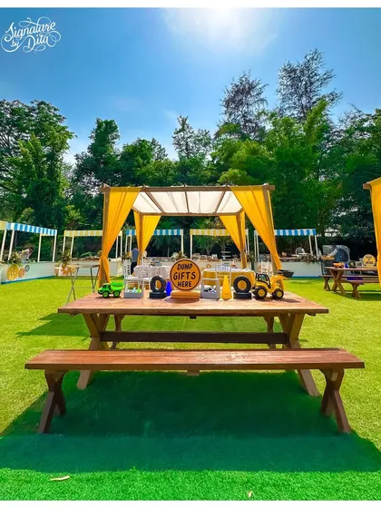 A picnic-style dining area for the construction party. The rustic wooden tables and benches are perfect for an informal outdoor meal, with a themed canopy in the background.