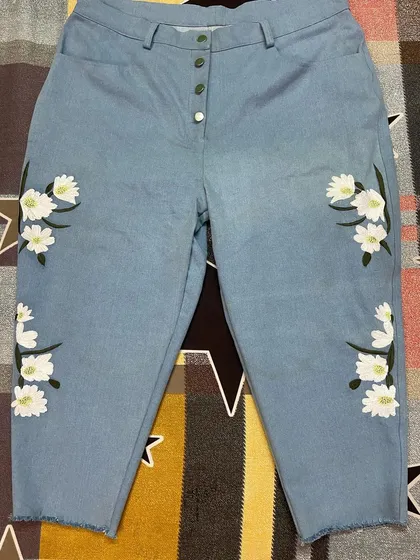 Bring your ideas to life with custom embroidery. These light-wash denim jeans feature a delicate floral design, a button fly, and a modern frayed hem, all tailored to exact measurements.