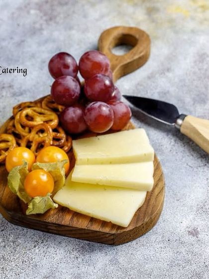 A minimalist cheese plate with sliced cheese, pretzels, grapes, and cape gooseberries, arranged on a small wooden board. Ideal for an individual serving or a small, intimate tasting.