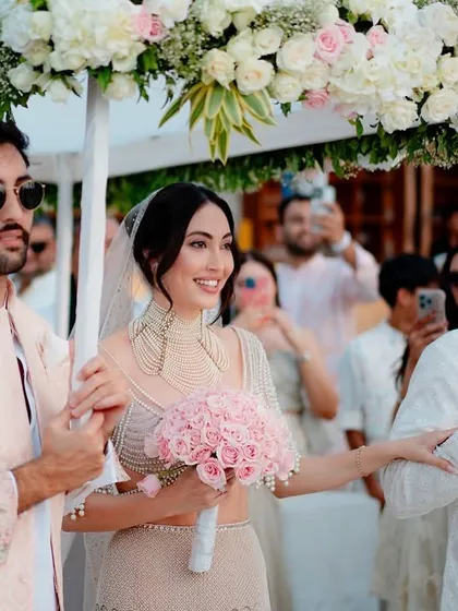 The bride's entrance under a floral canopy of white and pink roses, a classic and elegant choice for a beach wedding.
