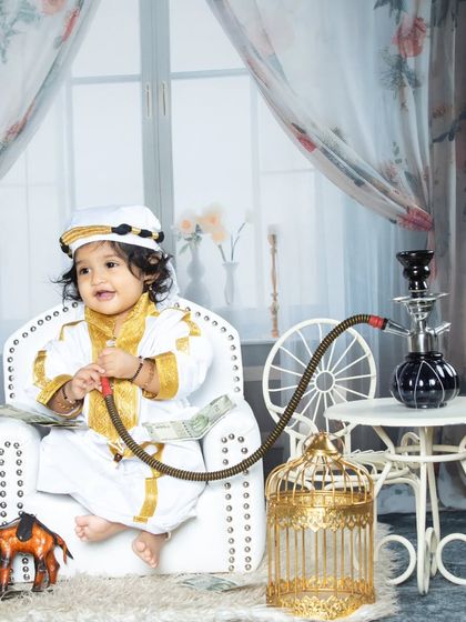 Our little sheikh is all smiles, enjoying the life of luxury. The golden birdcage and camel prop add to the opulent theme.