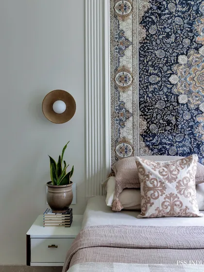 A unique take on a headboard, using an ornate, tapestry-like rug. This adds incredible texture, pattern, and a sense of history to the room, complemented by a modern brass wall sconce.