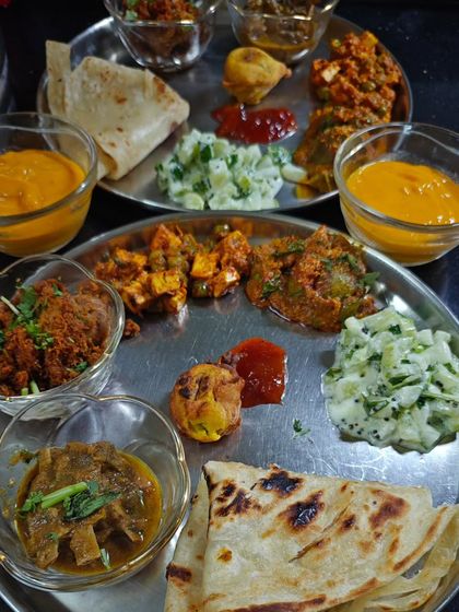 A thali from one of my dining experiences, where guests get to lick their fingers clean. This one had a mix of dishes like Bharlela Vanga, Kolhapuri Chicken Sukkha, and even Malabari Parotta. It’s all about enjoying the food without any hesitation.