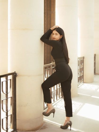 A full-body portrait showing a strong, confident pose against a pillar. The composition uses the repeating lines of the architecture to create a sense of rhythm and elegance.