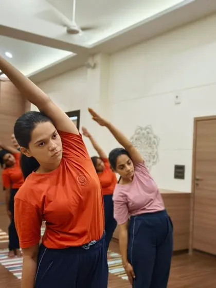 Students engage in a synchronized side stretch, a fundamental asana for improving spinal flexibility and posture. Our classes methodically move through postures to warm up and prepare the body safely.