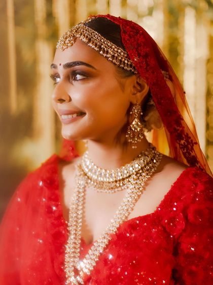 A beautiful close up of Aashna, glowing in her red Seema Gujral lehenga. Her makeup features soft, shimmery eyes and a perfectly blended base, creating a romantic and ethereal bridal look.