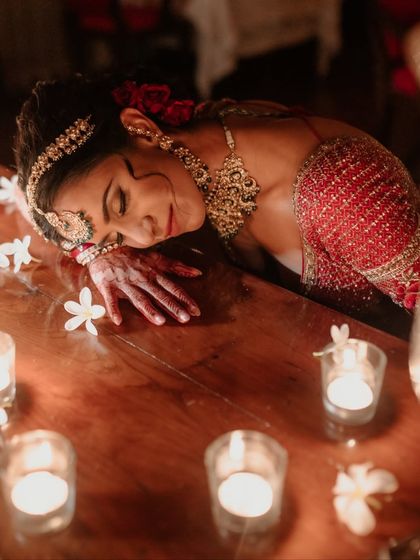 A serene and beautiful portrait of the bride resting on a candlelit table. The warm glow and scattered flowers create a deeply romantic and peaceful atmosphere at her Suryagarh wedding.