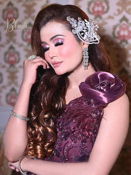 A beautiful engagement or cocktail party look. The focus is on the shimmery purple eyeshadow and glowing skin, paired with soft curls and a statement hairpiece.