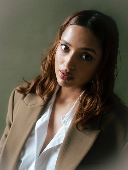 A warm and inviting close-up portrait. The direct gaze and soft lighting create a connection with the viewer, making it a very engaging and personal-feeling fashion shot.