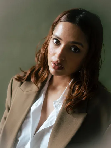 A warm and inviting close-up portrait. The direct gaze and soft lighting create a connection with the viewer, making it a very engaging and personal-feeling fashion shot.