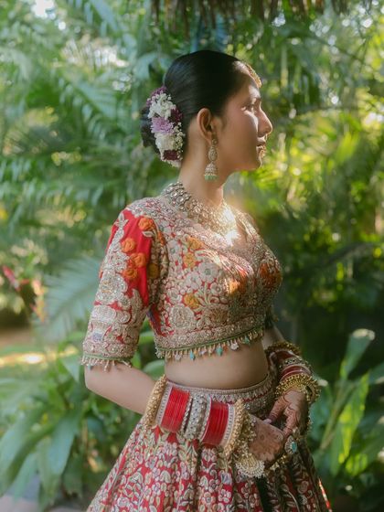 A side profile capturing the intricate details of the bride's hair, adorned with flowers, and the beautiful embroidery on her blouse.