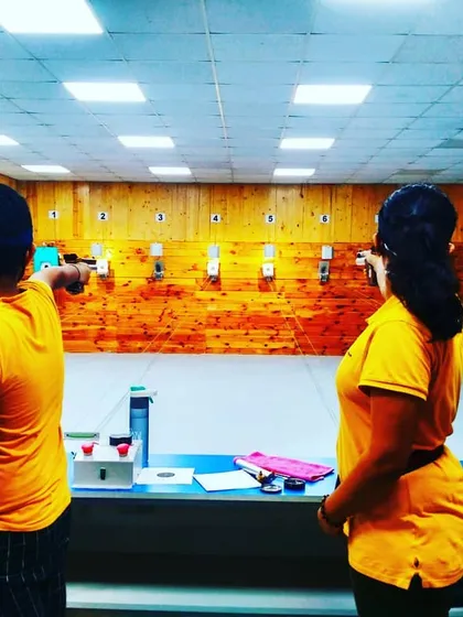 A back view of two students practicing with air pistols, showing their focused stance as they aim at the targets down the 10-meter range.