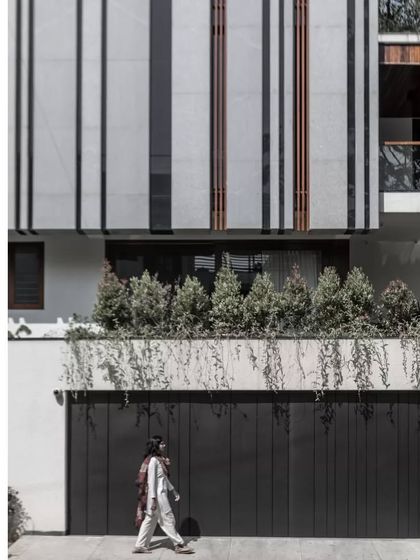 The Janani House facade features a striking pattern of vertical bands in grey and black, creating a strong graphic quality. A planter with cascading greenery softens the geometry of the building, adding a touch of nature to the urban setting.