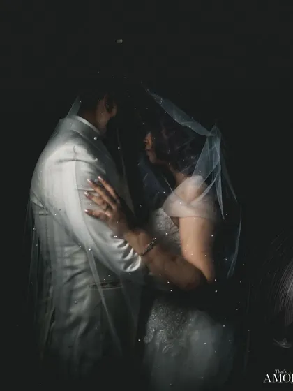 A classic, romantic portrait of a Christian bride and groom under the veil. The dark, moody lighting creates an intimate and timeless feel, focusing solely on their connection.