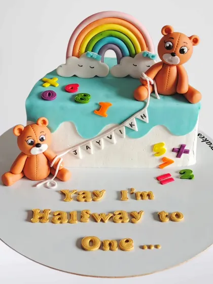 "Yay I'm Halfway to One!" This adorable half-birthday cake features two teddy bears, a rainbow, and colorful numbers, celebrating the six-month mark.