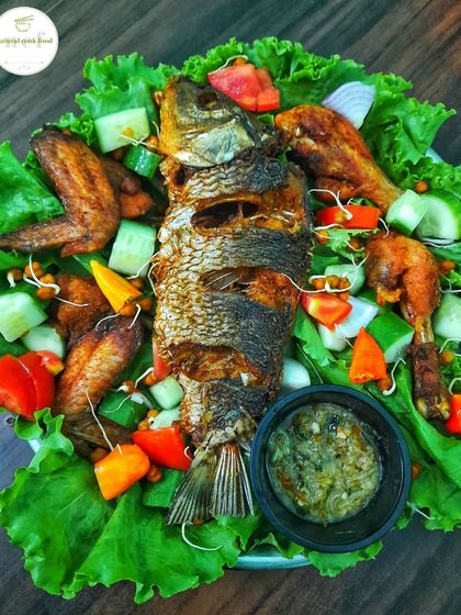 A beautiful platter featuring a whole deep-fried fish, chicken wings, and leg pieces, garnished with fresh veggies and served with my garlic and ginger chutney.