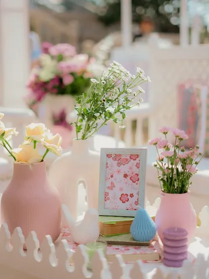 A close-up of a tablescape at the pastel Mehendi, featuring a collection of modern ceramic vases in pink and white, candles, and small bird figurines for a whimsical touch.