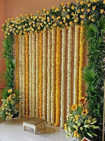 A classic and vibrant Haldi ceremony backdrop. This setup features curtains of yellow and white marigolds framed by lush greenery, creating a traditional and photogenic space.