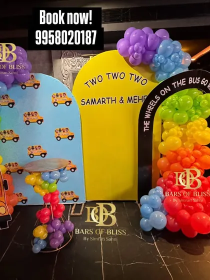 A colorful 'Wheels on the Bus' theme for a second birthday party. This fun setup features custom backdrops, a school bus cutout, and rainbow-colored balloon arrangements.