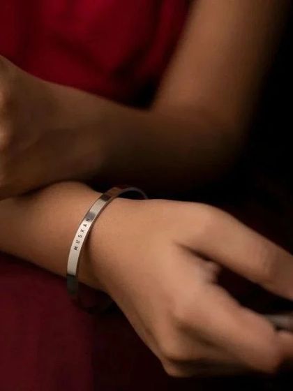 A woman wearing a silver cuff engraved with 'MUSKAN'. The simple elegance of the bracelet makes it a versatile piece for any occasion.