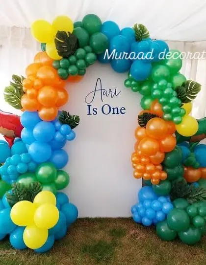 This vibrant dinosaur-themed balloon arch uses bright primary colors like blue, orange, green, and yellow. We added dinosaur head props and tropical leaf accents to complete the jurassic look for a fun first birthday.