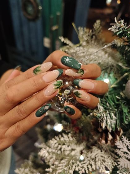 A gorgeous Christmas-themed manicure featuring matte green polish with hand-painted pine trees and delicate snowflakes.