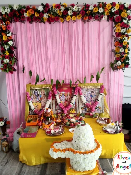 The complete altar setup for the Ramayan ceremony. The pink backdrop is framed with a garland of fresh, colorful flowers.