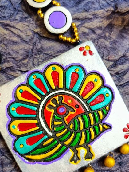 A close-up of the square block-printed peacock pendant. You can see the texture of the print and the small, hand-painted floral details in the corners.