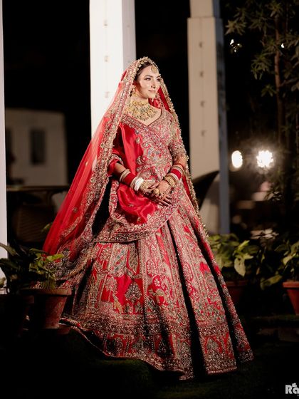 A full-length outdoor portrait of the bride in her stunning red lehenga. The night-time setting with soft background lights adds a magical quality to this beautiful bridal shot.