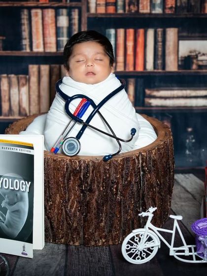 A classic 'future doctor' pose, with the newborn swaddled and surrounded by books, showcasing their potential.