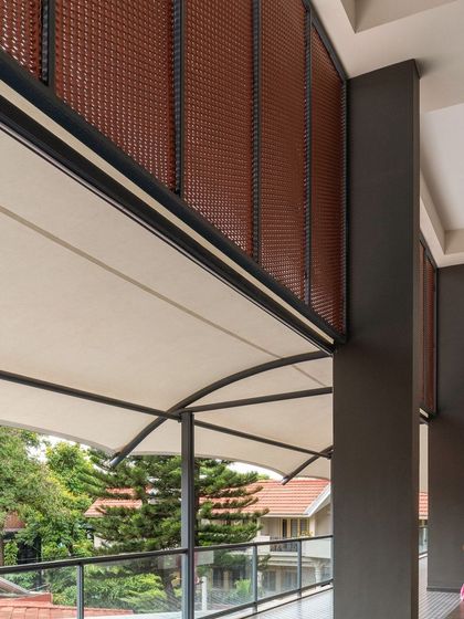 A view from an upper-level corridor in the Koramangala Club Annexe. A retractable awning and perforated screens help manage sunlight and create comfortable, shaded walkways that overlook the surrounding greenery.
