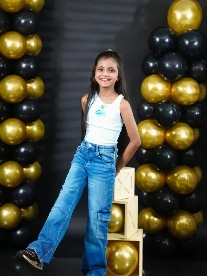 A classic, smiling portrait of the birthday girl standing between festive black and gold balloon columns.