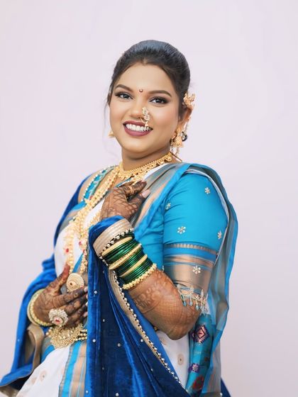 A full view of the bride's white and blue saree look, complete with green bangles and traditional gold jewellery.