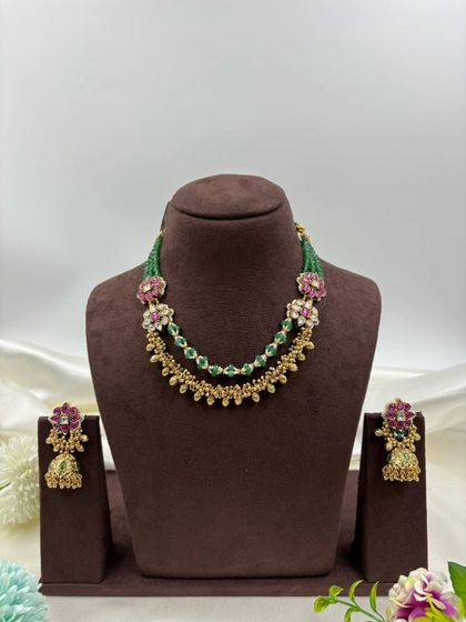 The Rishika premium antique gold set. It features a unique double-layer design with one layer of golden beads and another of green beads, adorned with floral motifs in pink stones.