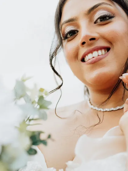 A joyful close-up of the bride. This shot captures her radiant smile and the flawless, glowing finish of her makeup, perfect for a beachside wedding.