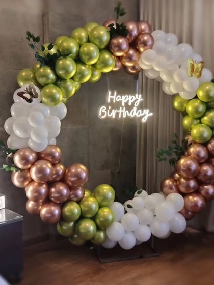 A first birthday decoration with a full ring of balloons in green, rose gold, and white, a central neon sign, and a "1" marquee number.