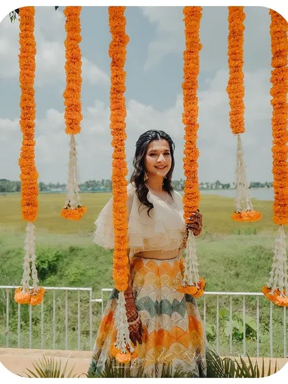Our client enjoying her outdoor ceremony, framed by marigold decorations. Her multi-colored lehenga and airy cape blouse are perfect for a sunlit celebration.
