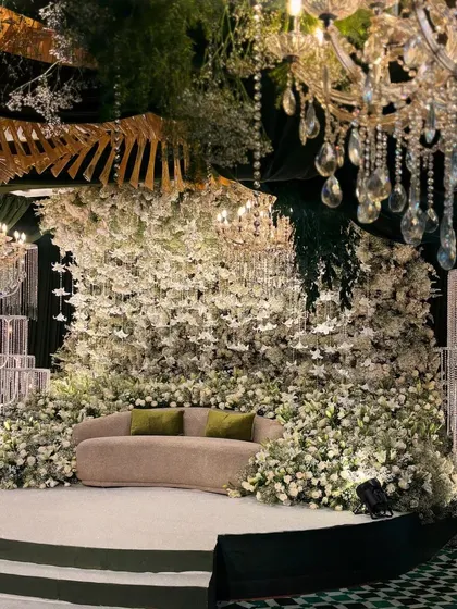 I designed this pristine white stage for a Sangeet, creating an enchanted forest feel. The seating is nestled within a massive wall of thousands of white flowers and foliage, illuminated by elegant crystal chandeliers for a truly magical ambiance.