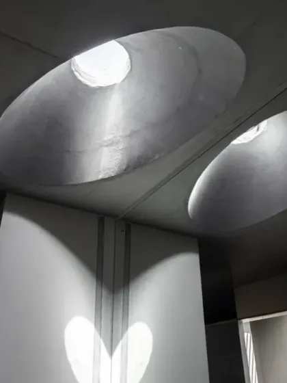The interplay of light from multiple circular skylights creates overlapping patterns on the walls and floor. This dynamic effect changes throughout the day as the sun moves across the sky.